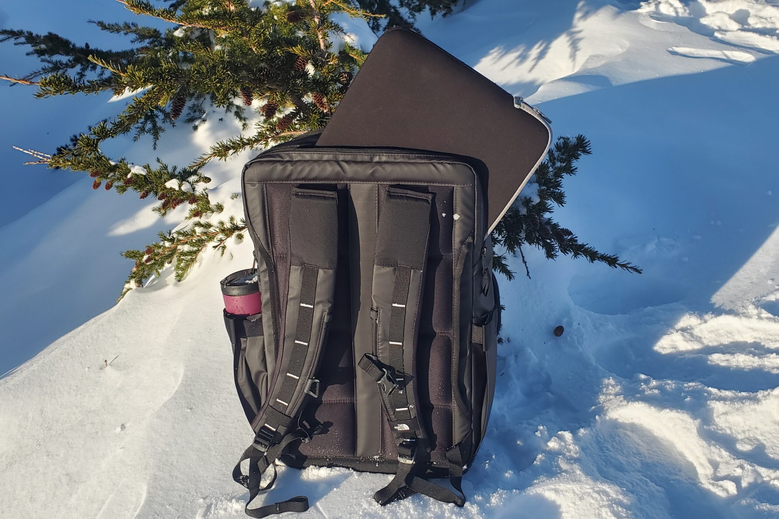 A backpack sits in the snow displaying the laptop compartment.