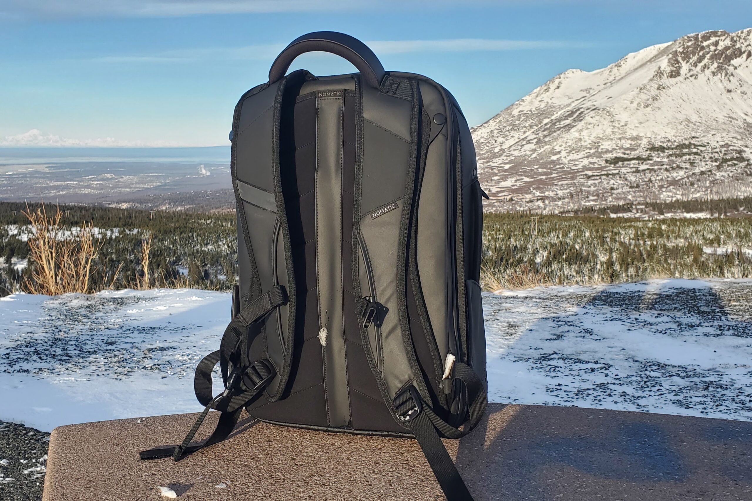 A backpack rests on a bench with a mountain landscape in the background.