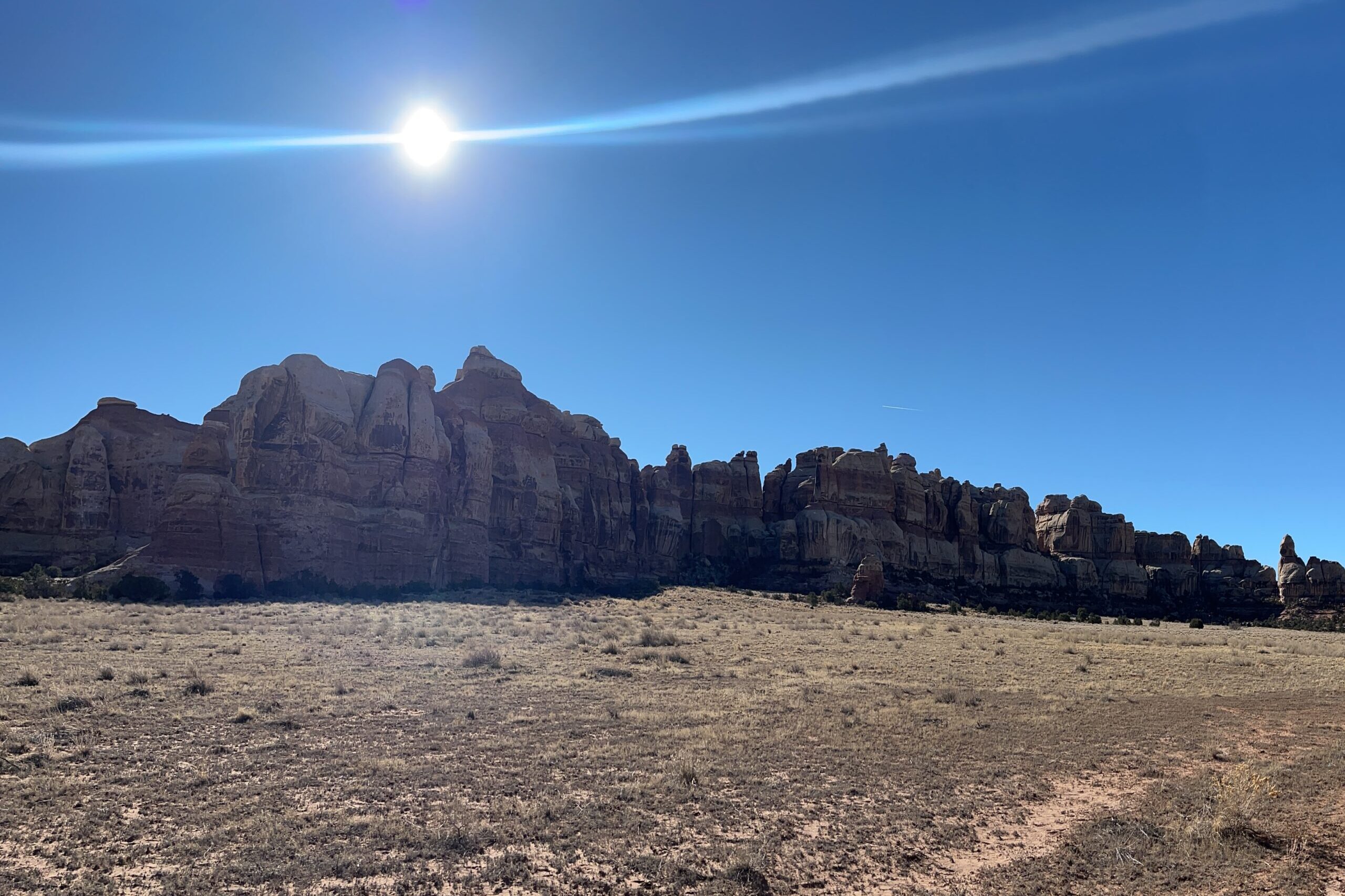 The sun shines directly above towering red rocks on a cloudless day in Canyonlands National Park