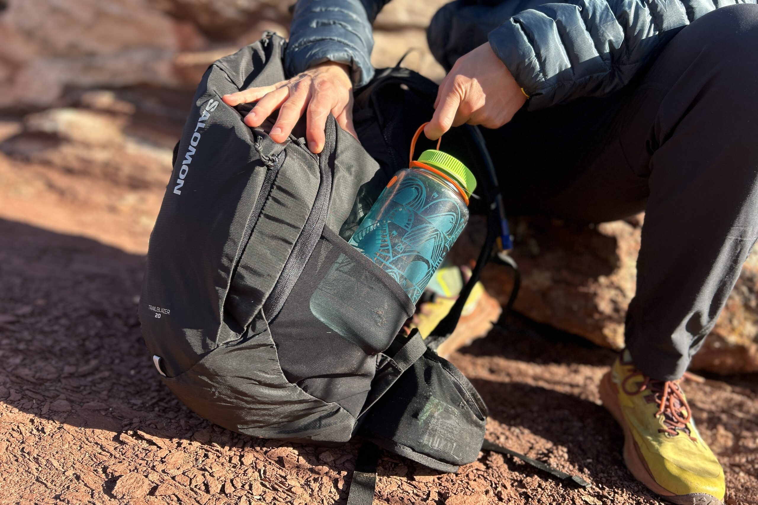 Close-up image of a person pulling a water bottle otu of the side pocket of a daypack.