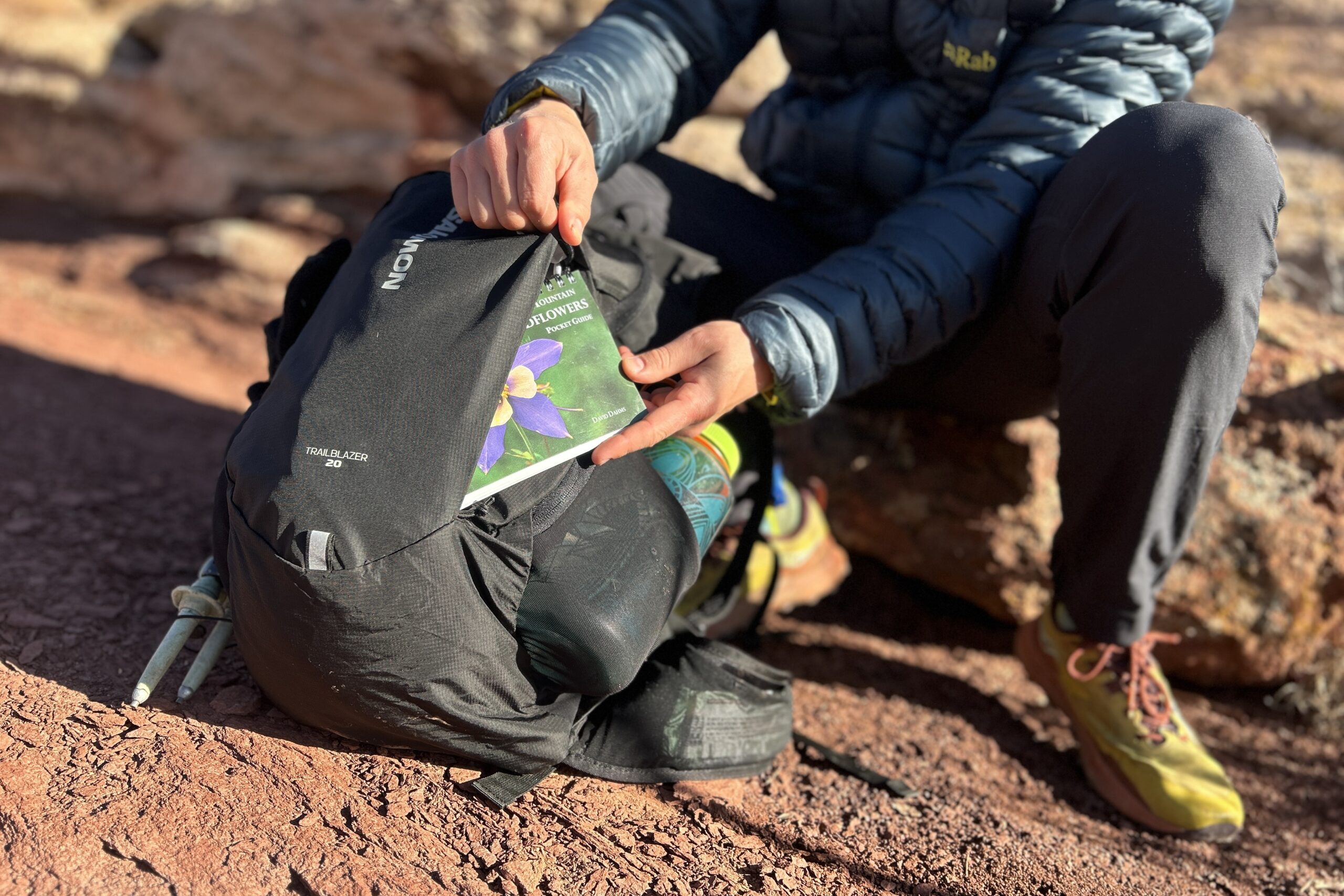 Close-up image of a person pulling a small wildflower guidebook out of the front pocket of a daypack.