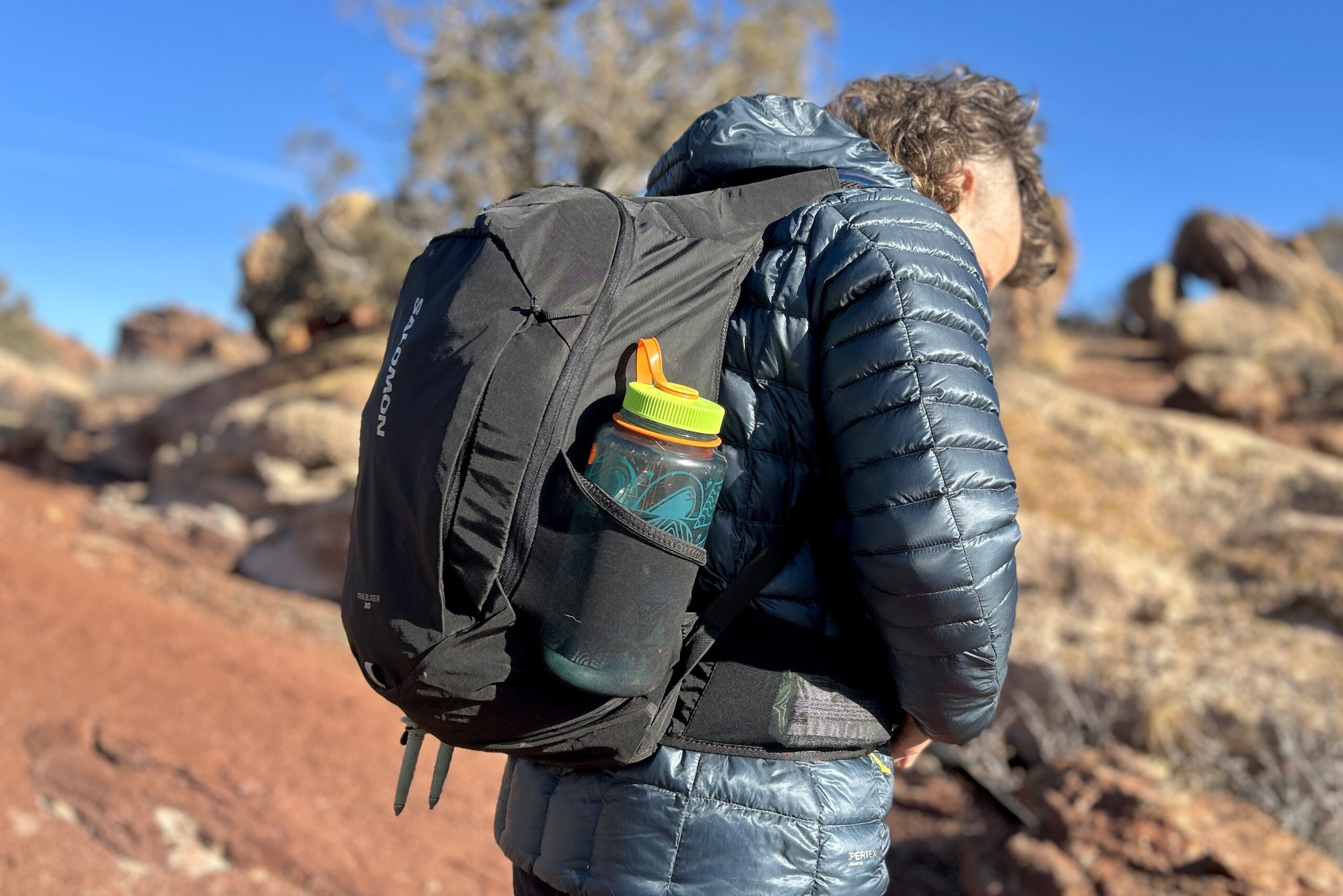 Close-up image from behind of a man adjusting a daypack, showing off the profile of the bag.