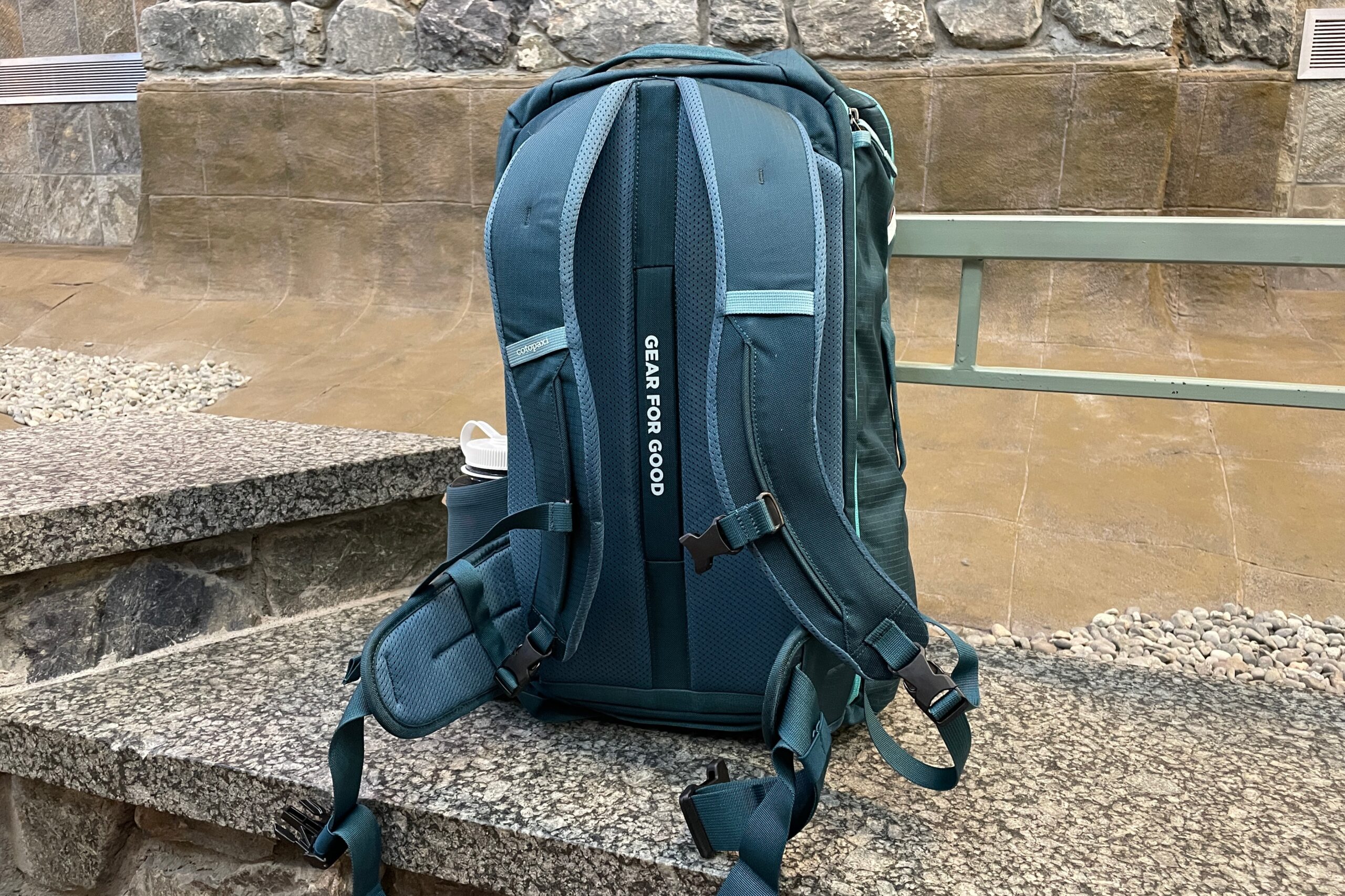 A green backpack sits on a marble bench.