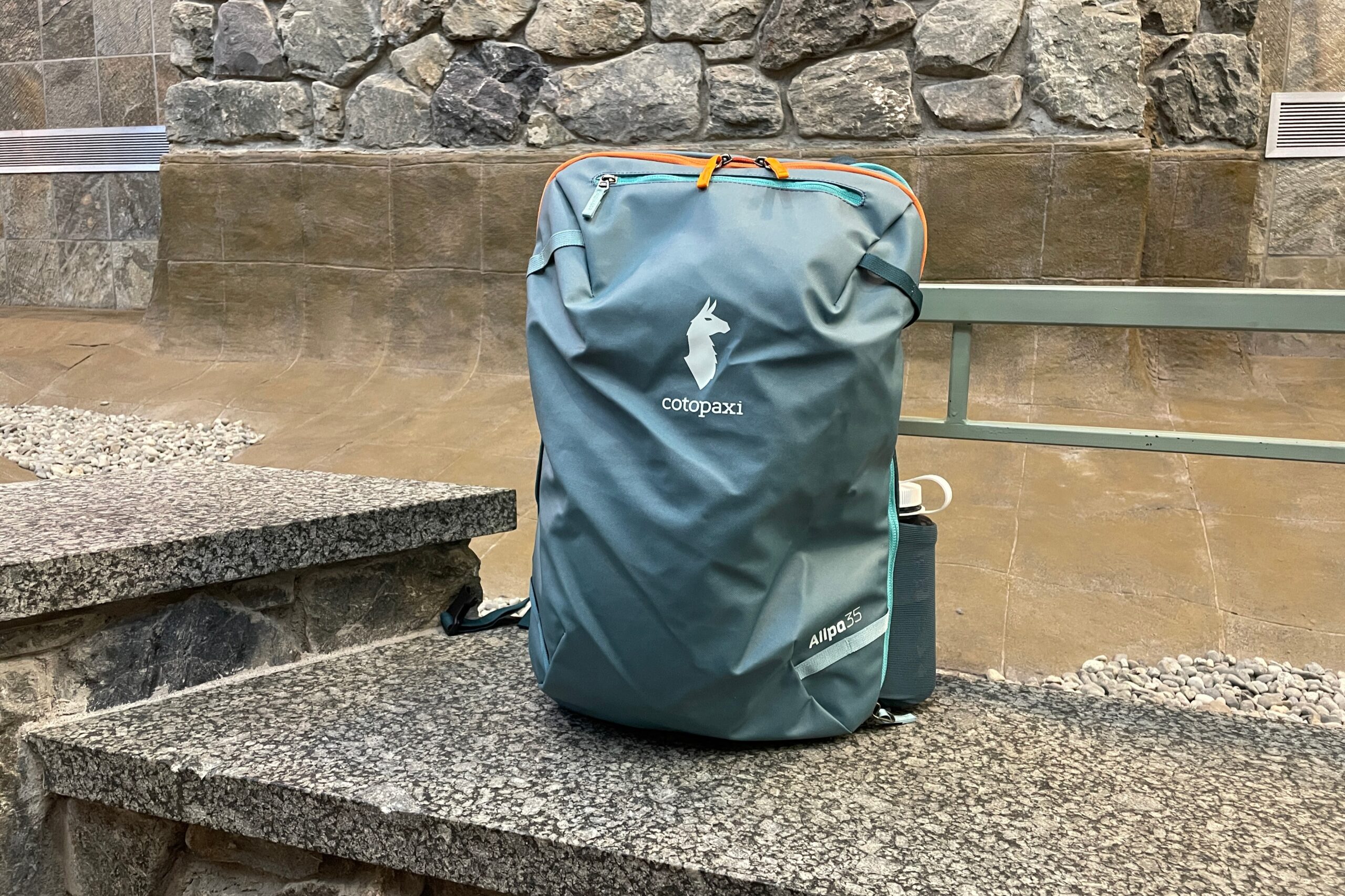 A green backpack sits on a marble bench with the exterior facing the camera.