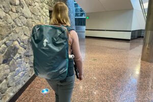 A woman walks through an airport wearing a travel backpack.