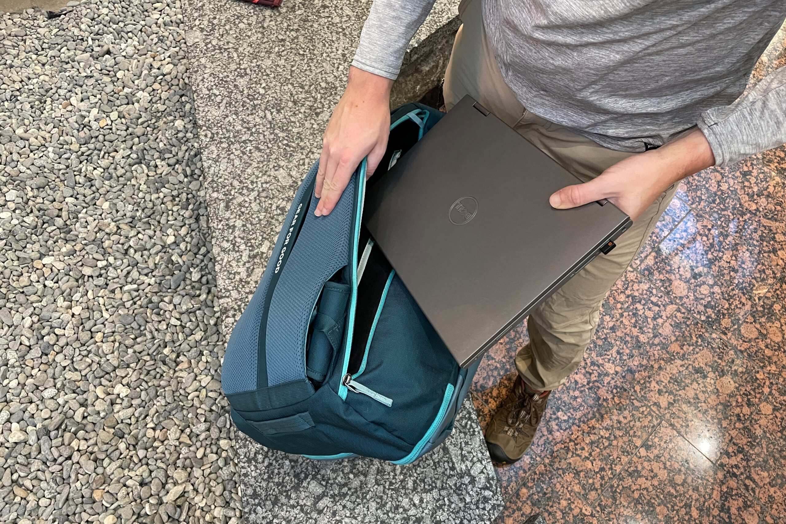 A man slides a laptop into the compartment of a backpack.