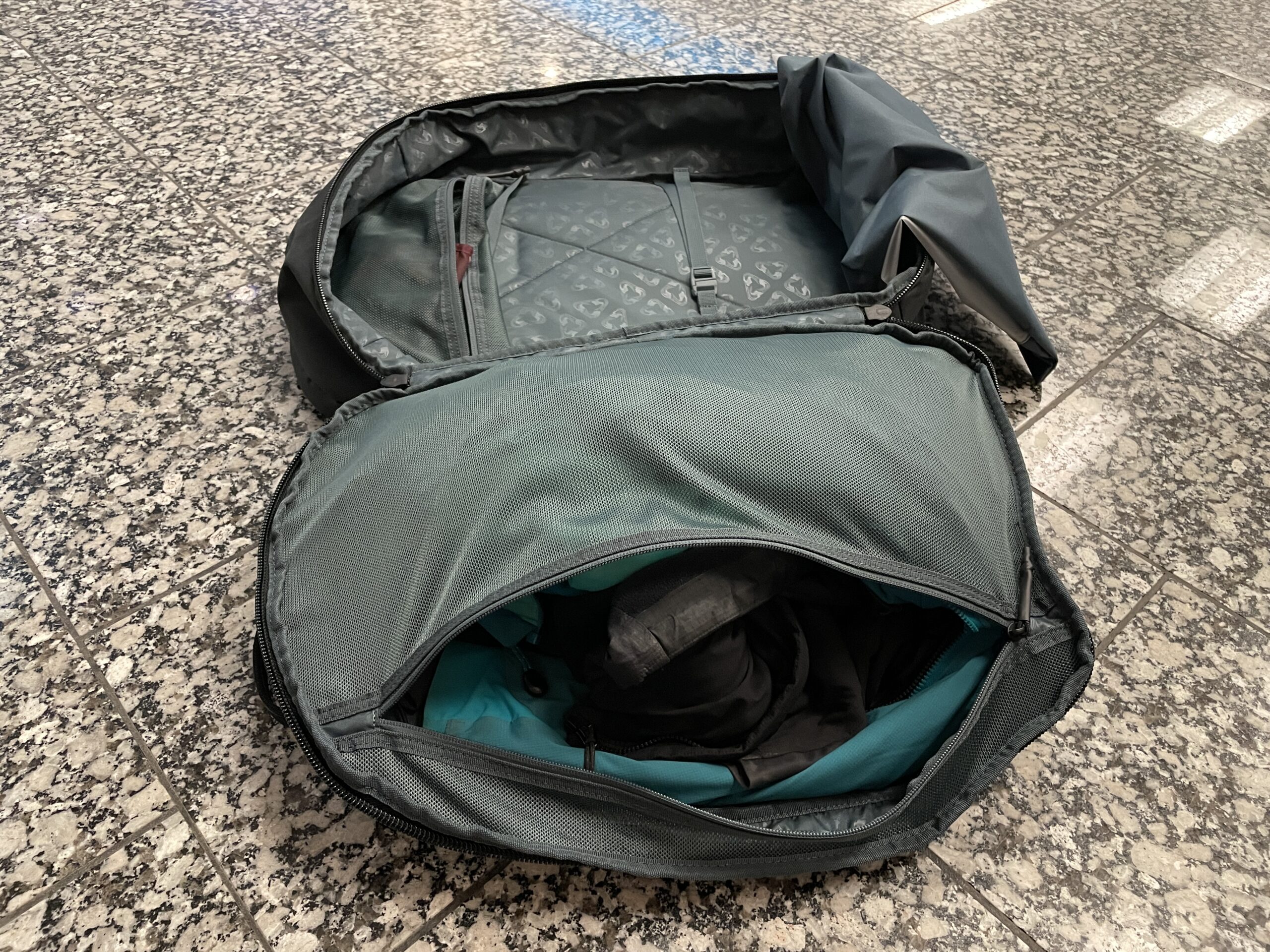 A backpack sits on the floor fully unzipped and open.