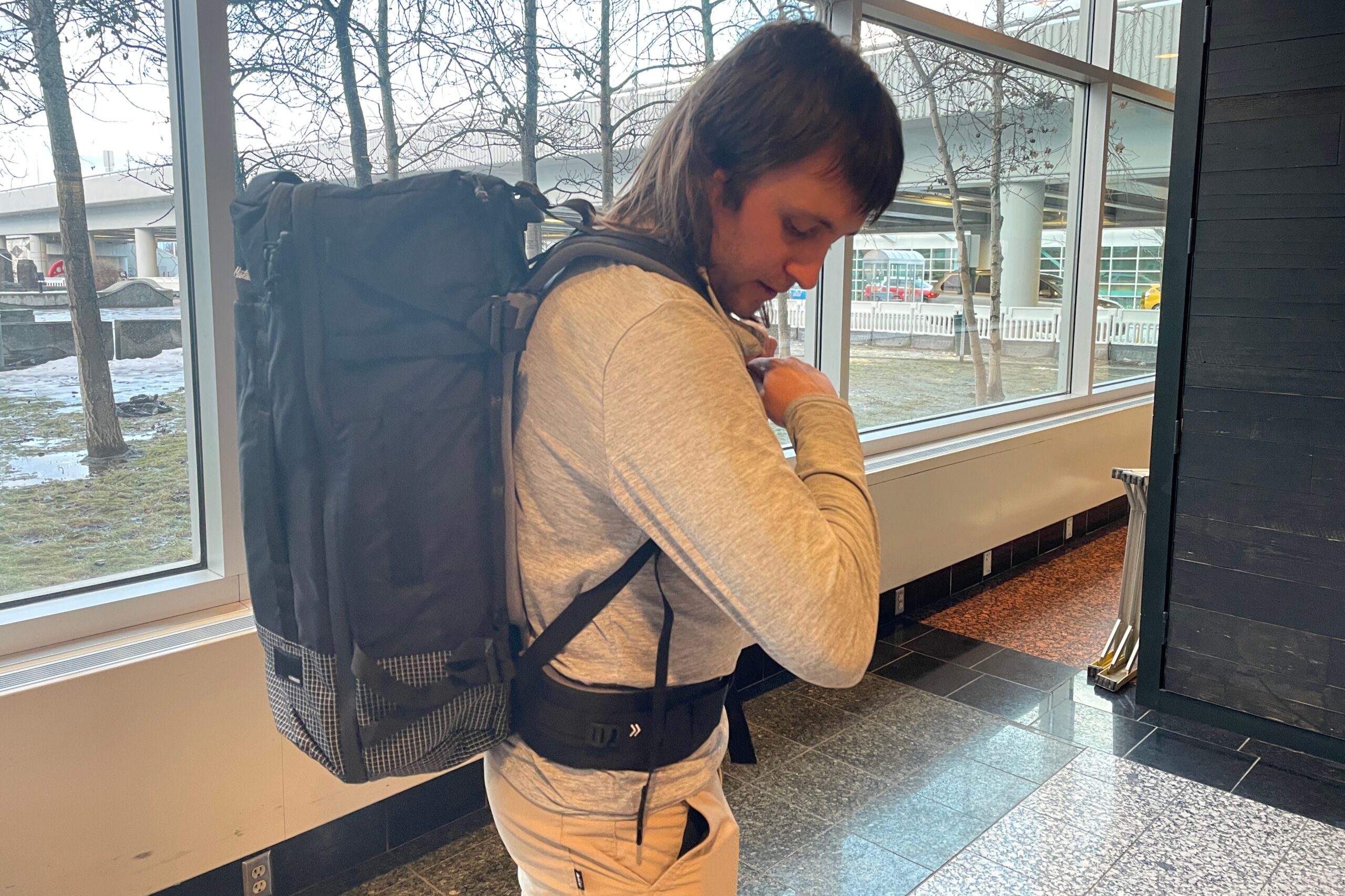 A man adjusts the strap on a backpack in the airport.