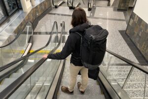 A man rides an escalator down through an airport.