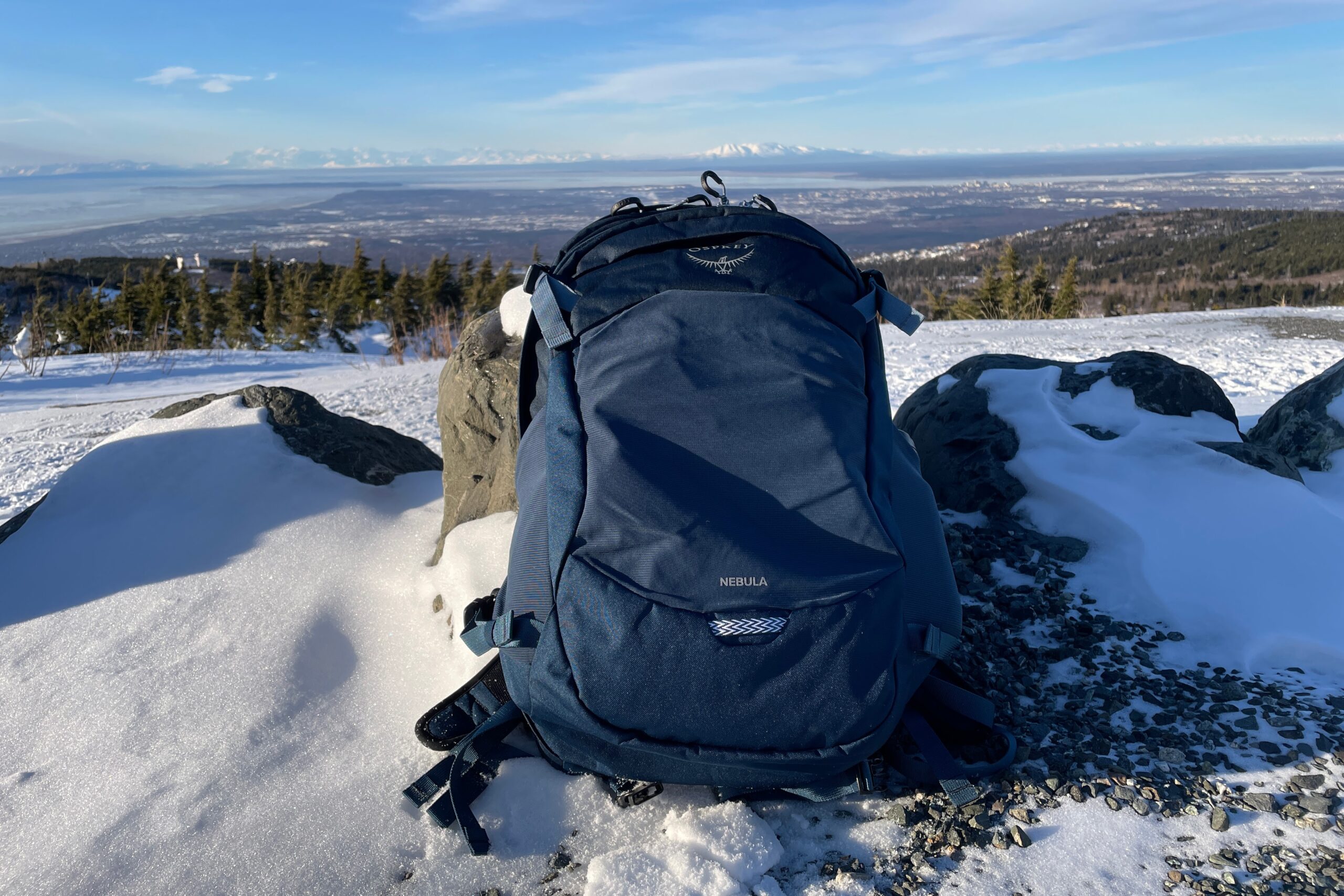 A blue backpack rests against a rock with a mountain view.