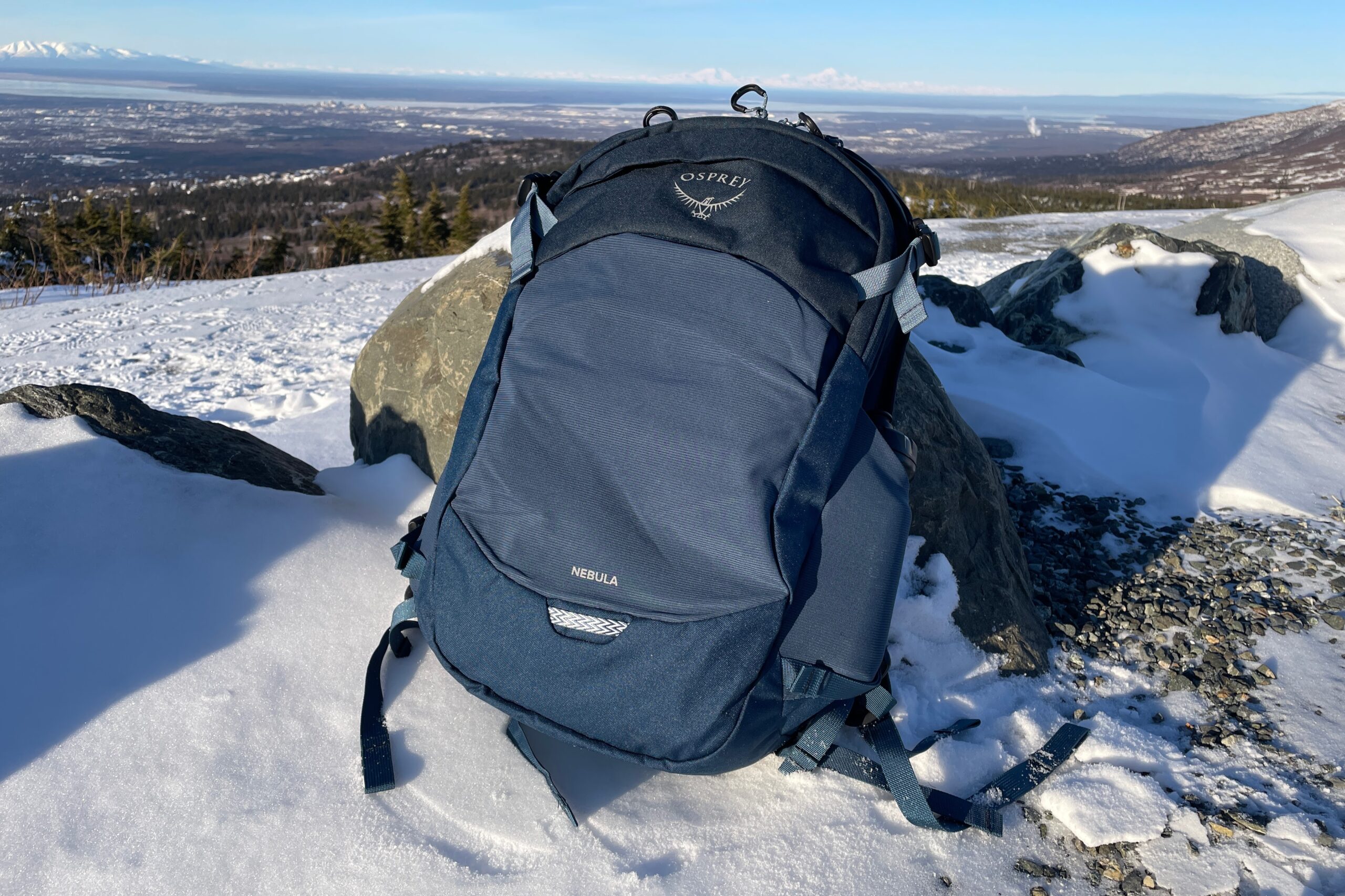 A blue backpack rests against a rock with a mountain view.