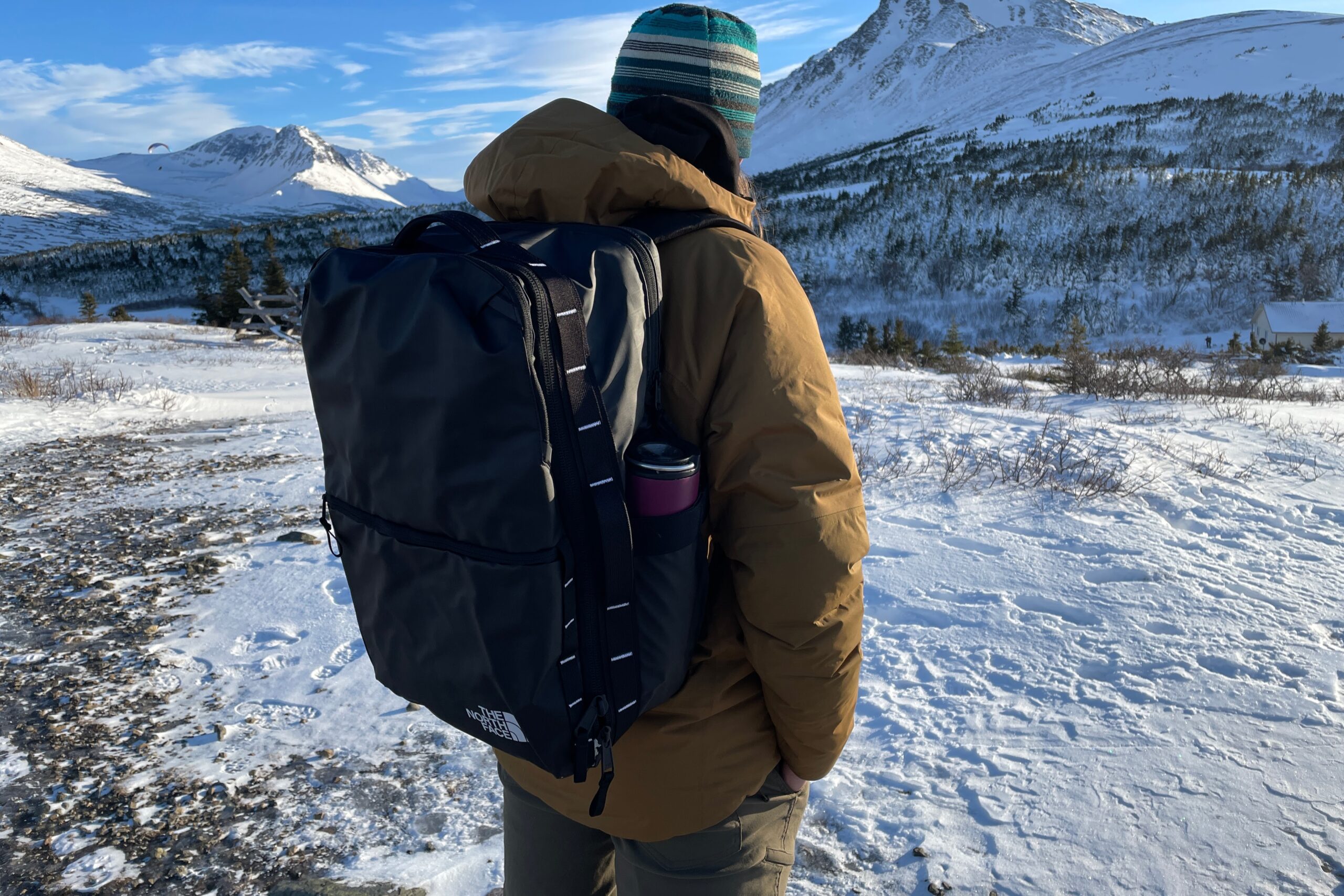 A man wearing a black backpack faces away from the camera.