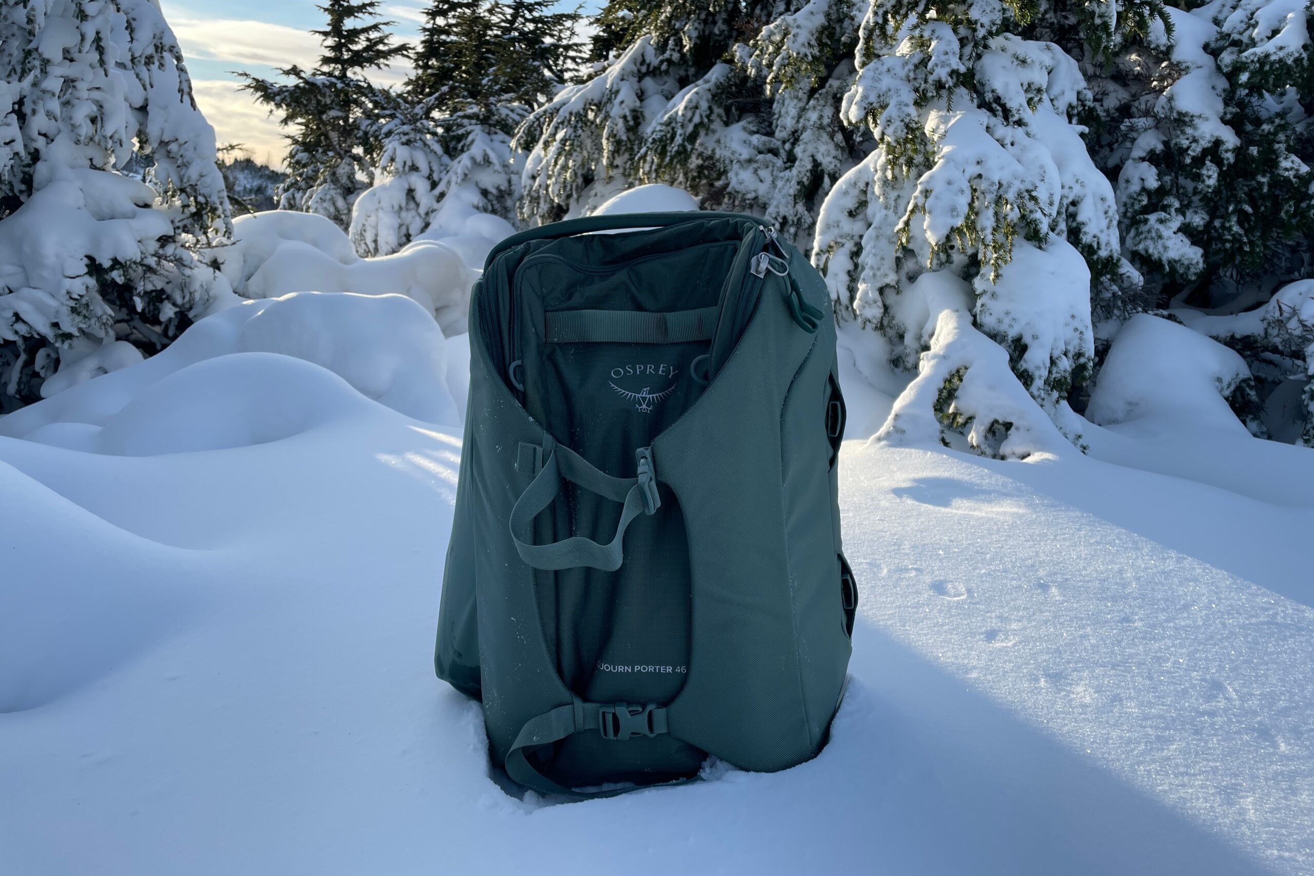 A green backpack sits on the ground in a snowy meadow.