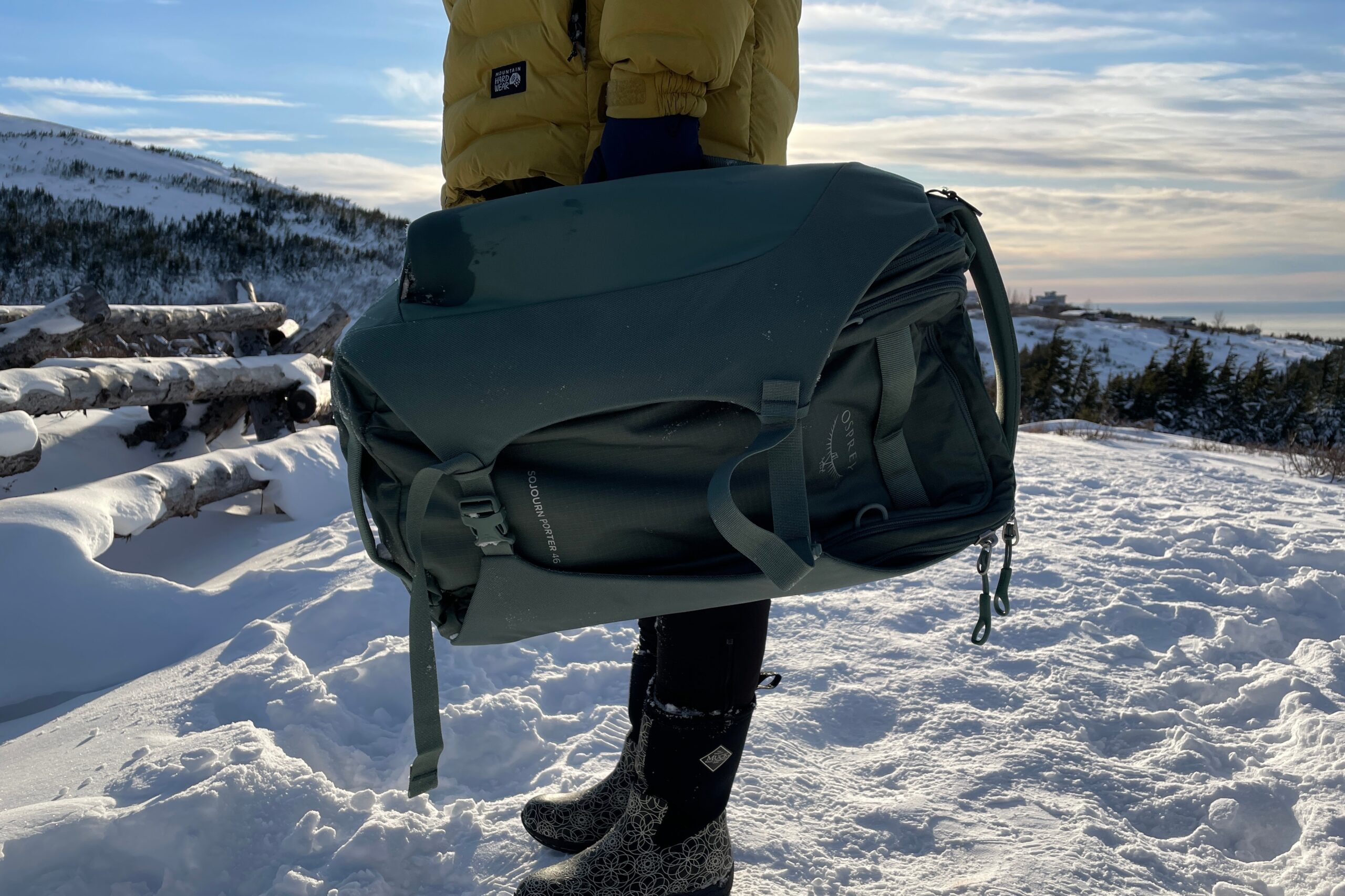 A woman carries a bag by it's side handle on a snowy trail.