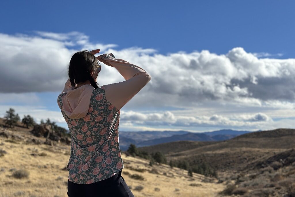 Woman in floral sun shirt looking out at view of foothills in high desert detting